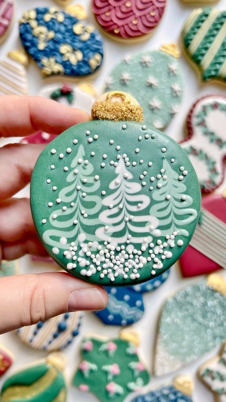 Green sugar cookie decorated with white icing trees held over other holiday cookies.