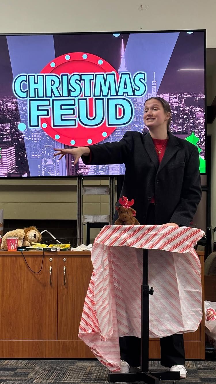 Woman gesturing toward a screen displaying Christmas Feud during a holiday party game.