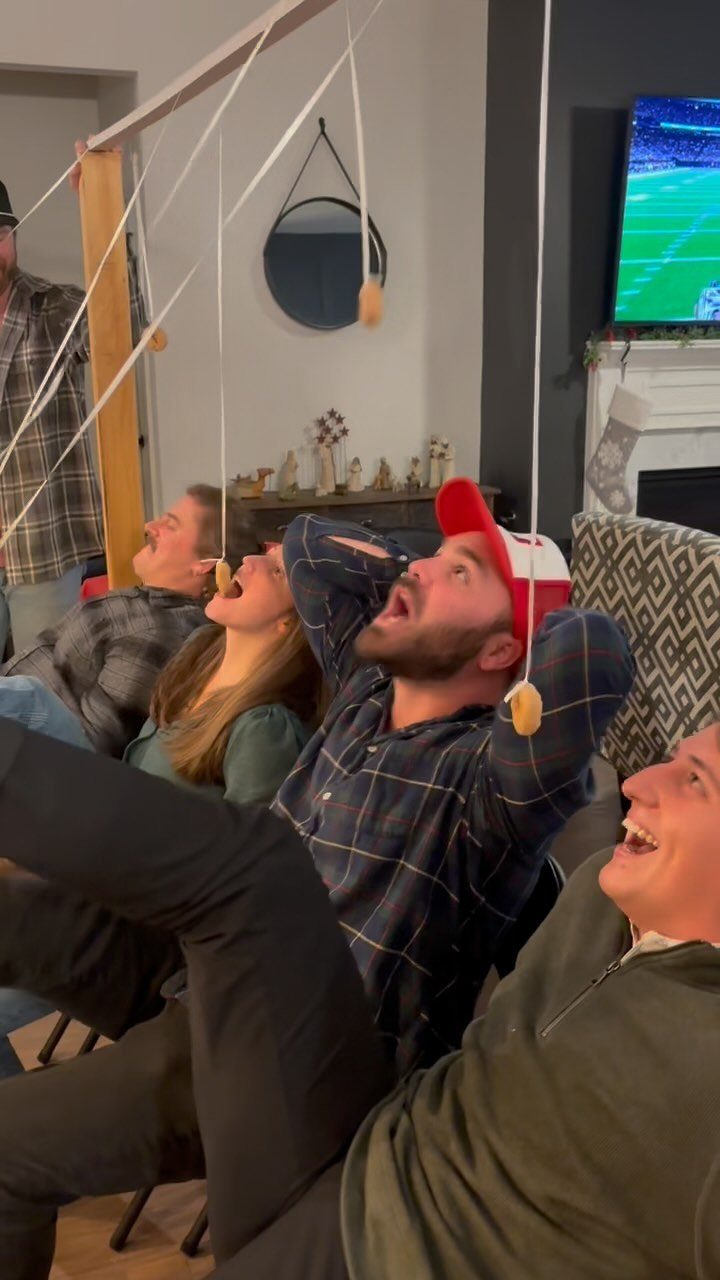 People leaning back to eat donuts hanging from strings during a party game.