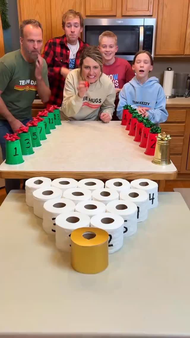 People reacting to a Christmas party game using numbered toilet paper rolls and cups.