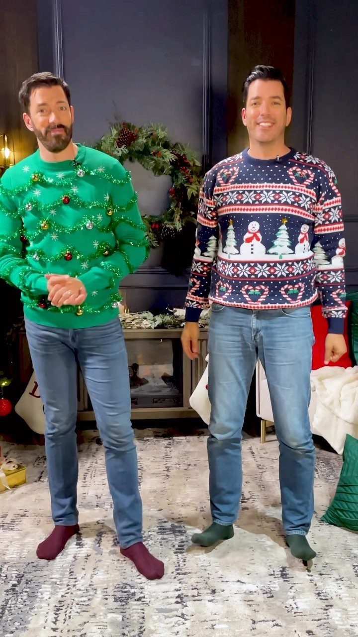 Two men wearing festive, tacky Christmas sweaters standing in a decorated room.