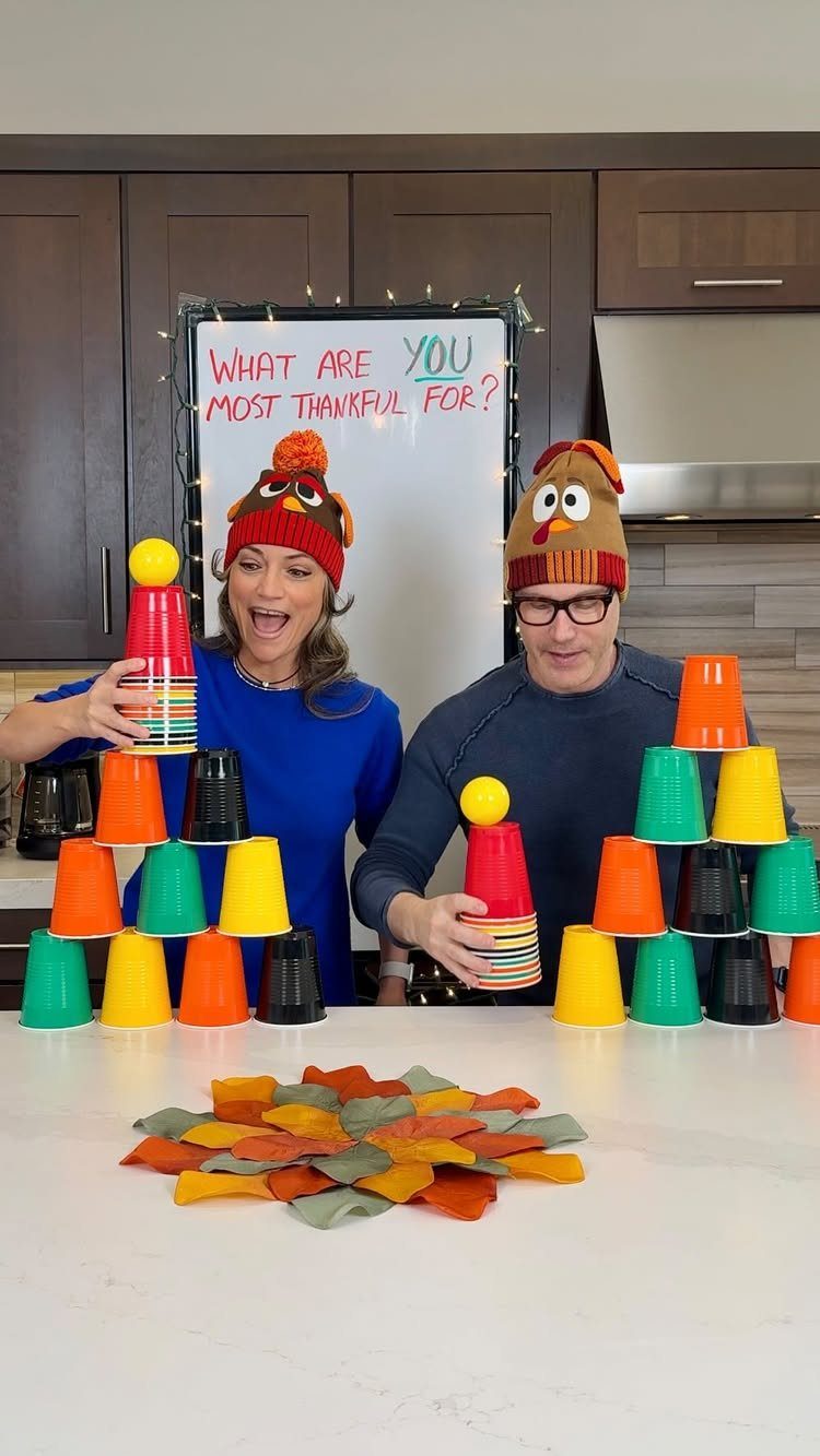 Man and woman in turkey hats playing a cup stacking game with autumn leaves.