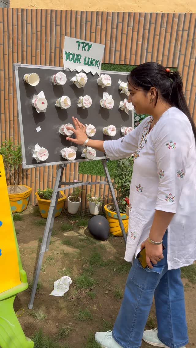 Woman playing a carnival-style game with white cups on a black board outdoors.