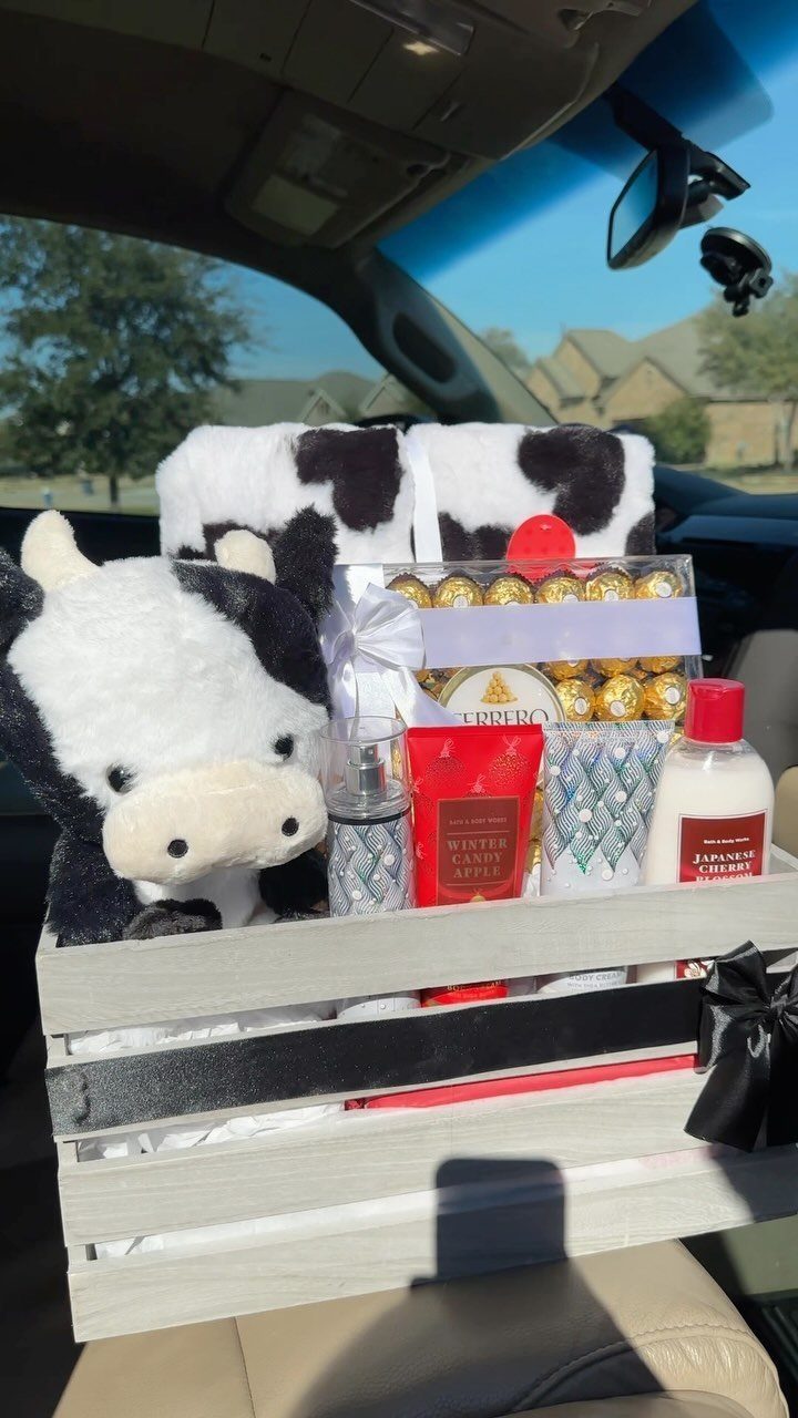 Cow-themed gift basket with plush toy and treats inside a white wooden crate.