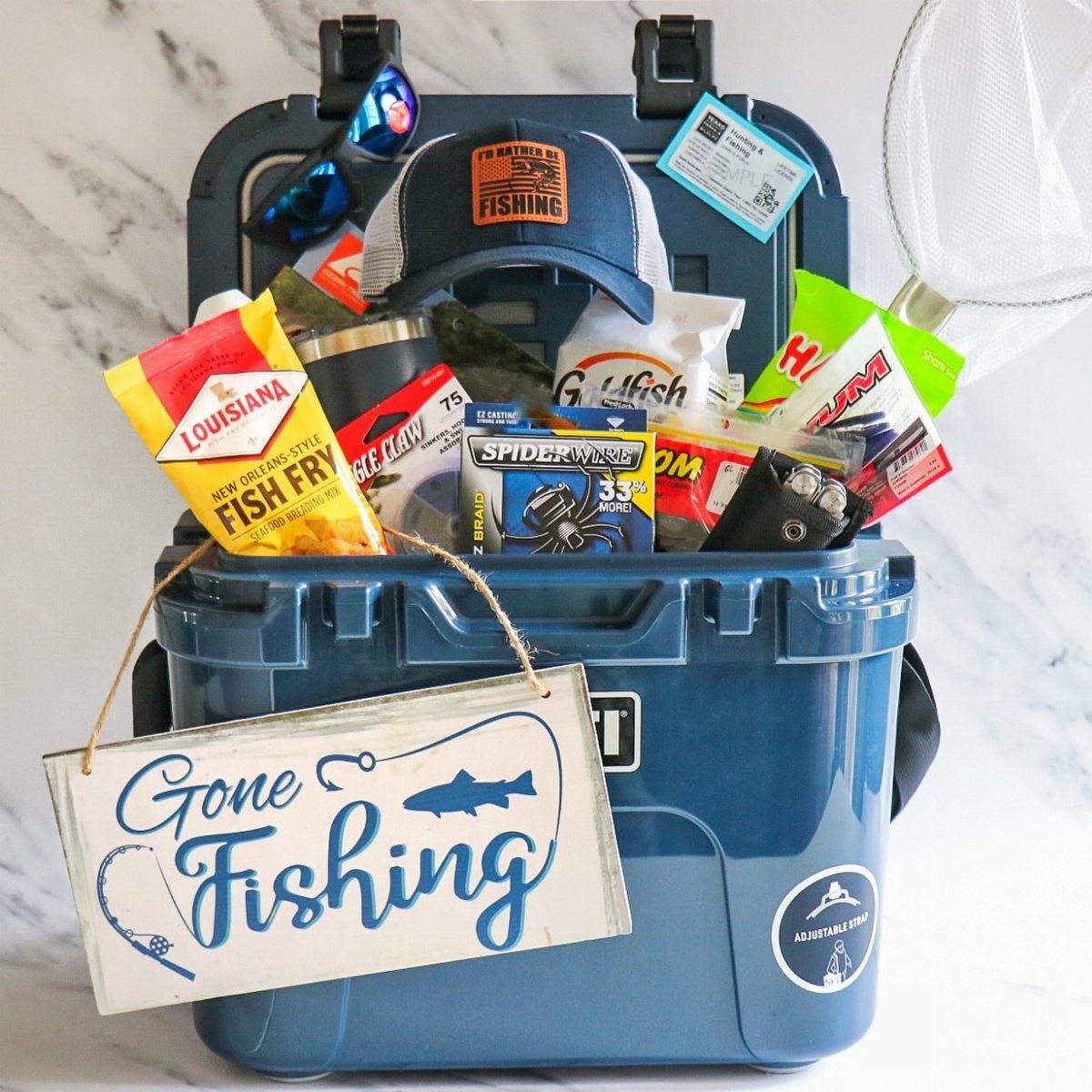 Fishing themed gift basket inside a blue cooler with gear and a sign.