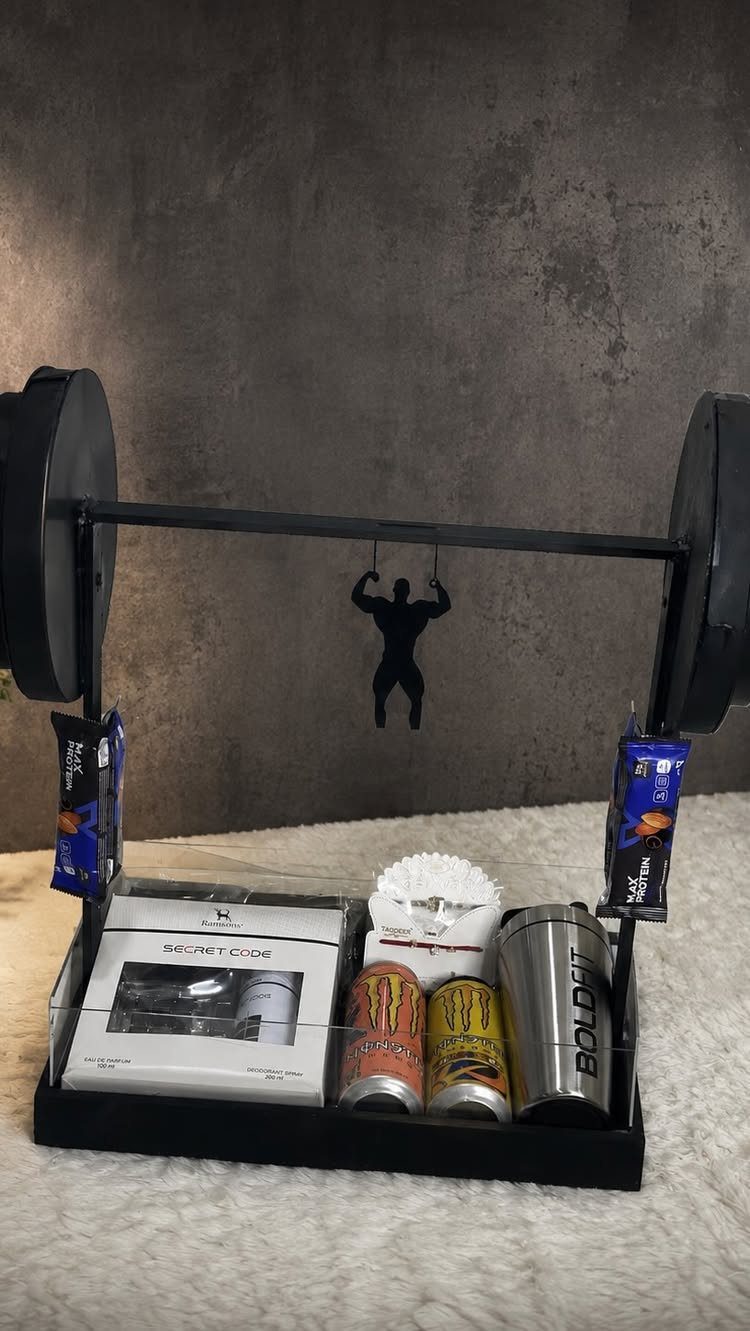 Fitness gift set with barbell frame, energy drinks, and a silver tumbler.