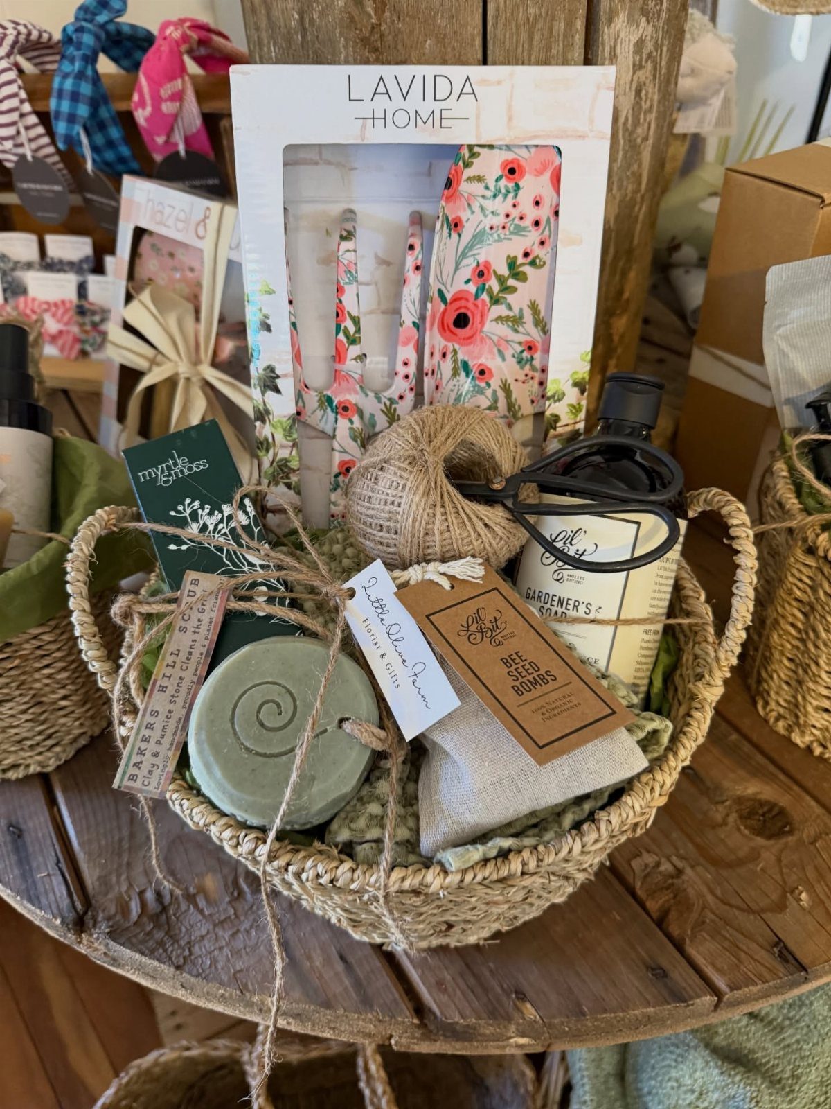 Woven gift basket with gardener's soap, floral towel, and green soap on wood.
