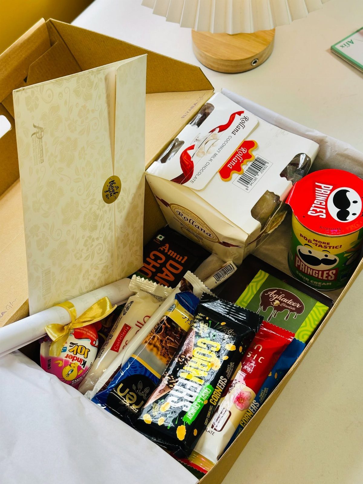 Cardboard gift box filled with Pringles, chocolate bars, and a greeting card.