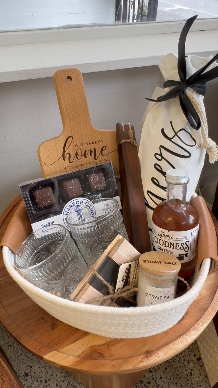 Gift basket filled with a wooden board, chocolates, glassware, and gourmet food items.