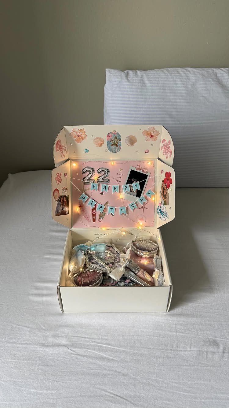 Open white gift box filled with beauty products and birthday decorations on a bed