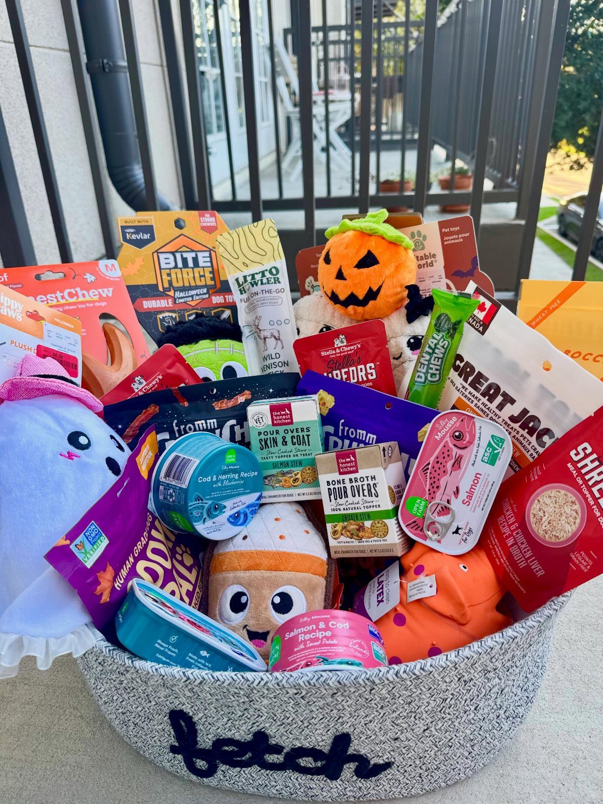 Grey fabric basket filled with colorful dog treats and plush pet toys.