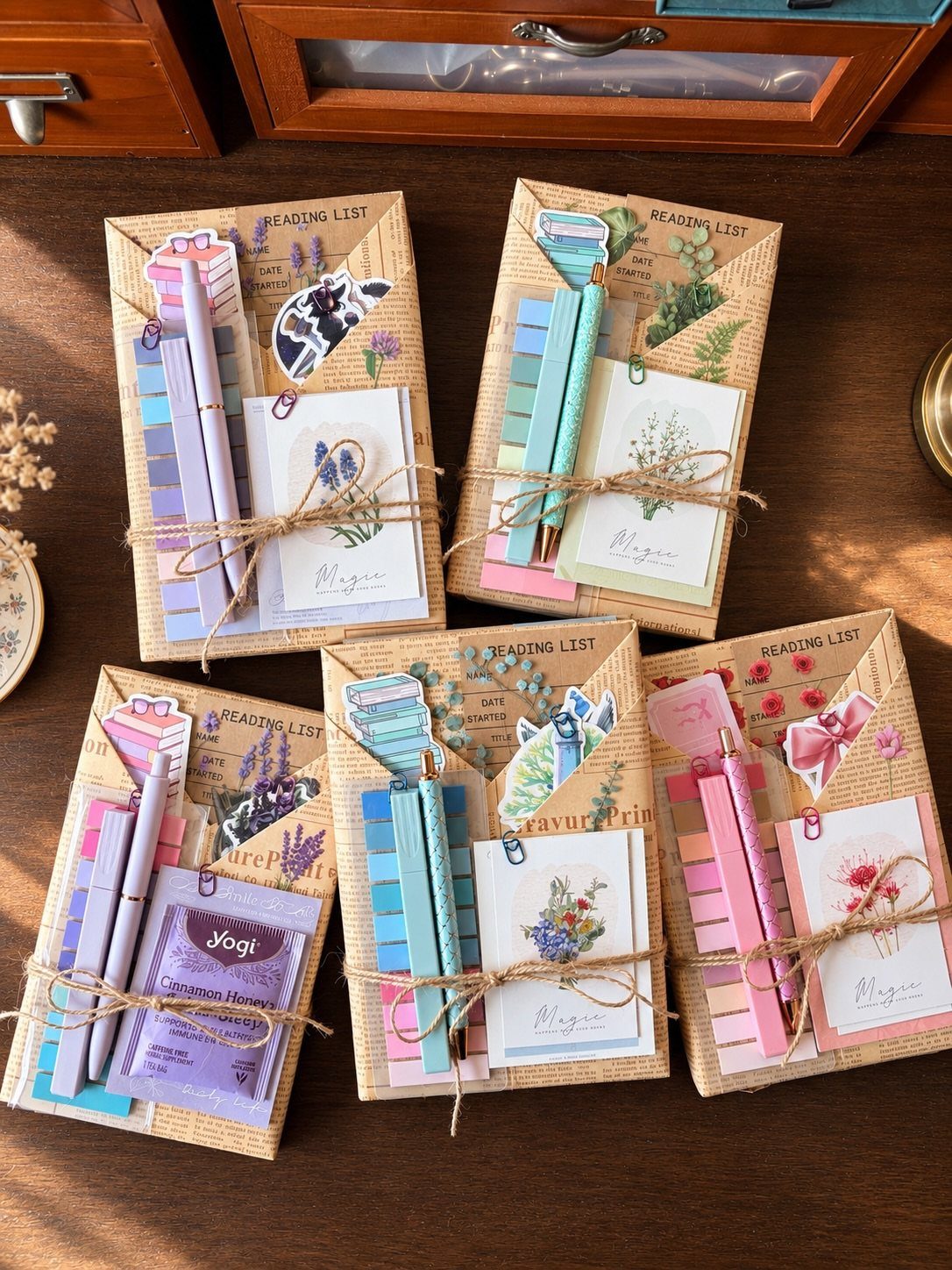 Four stationery gift sets with notebooks, pens, and stickers tied with twine on wood.