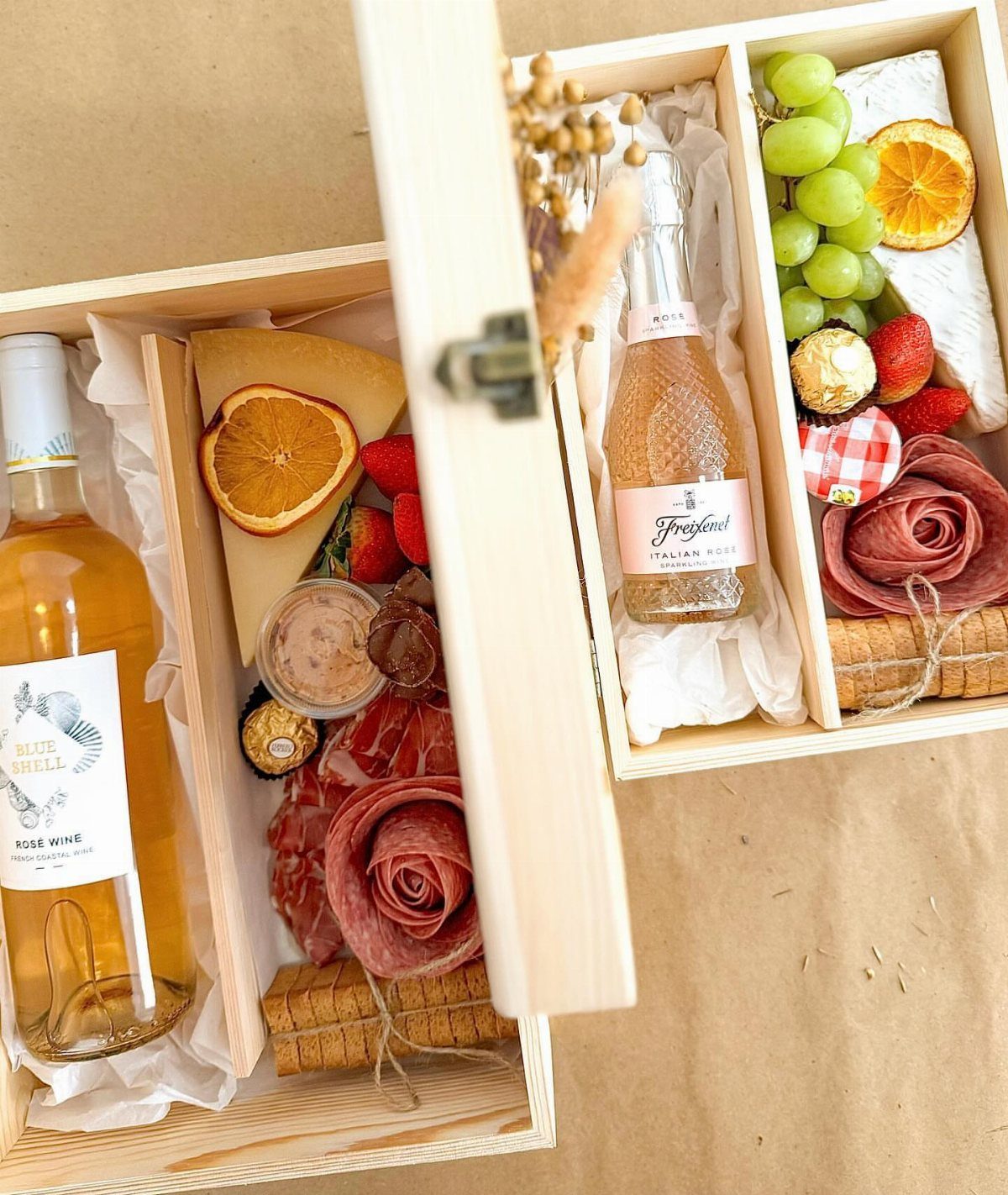 Wine and cheese gift boxes with cured meats, grapes, and dried fruit slices.