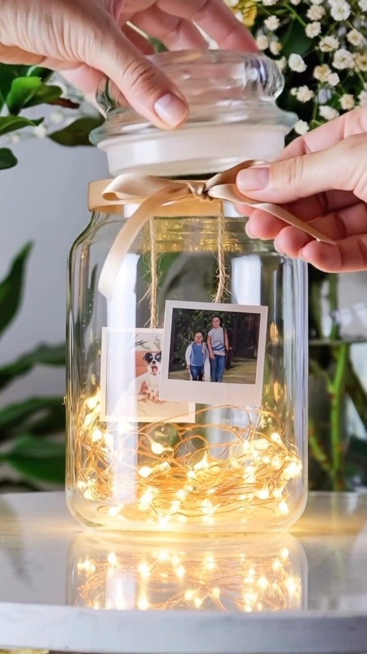 Glass jar with fairy lights and photographs tied with a beige ribbon.