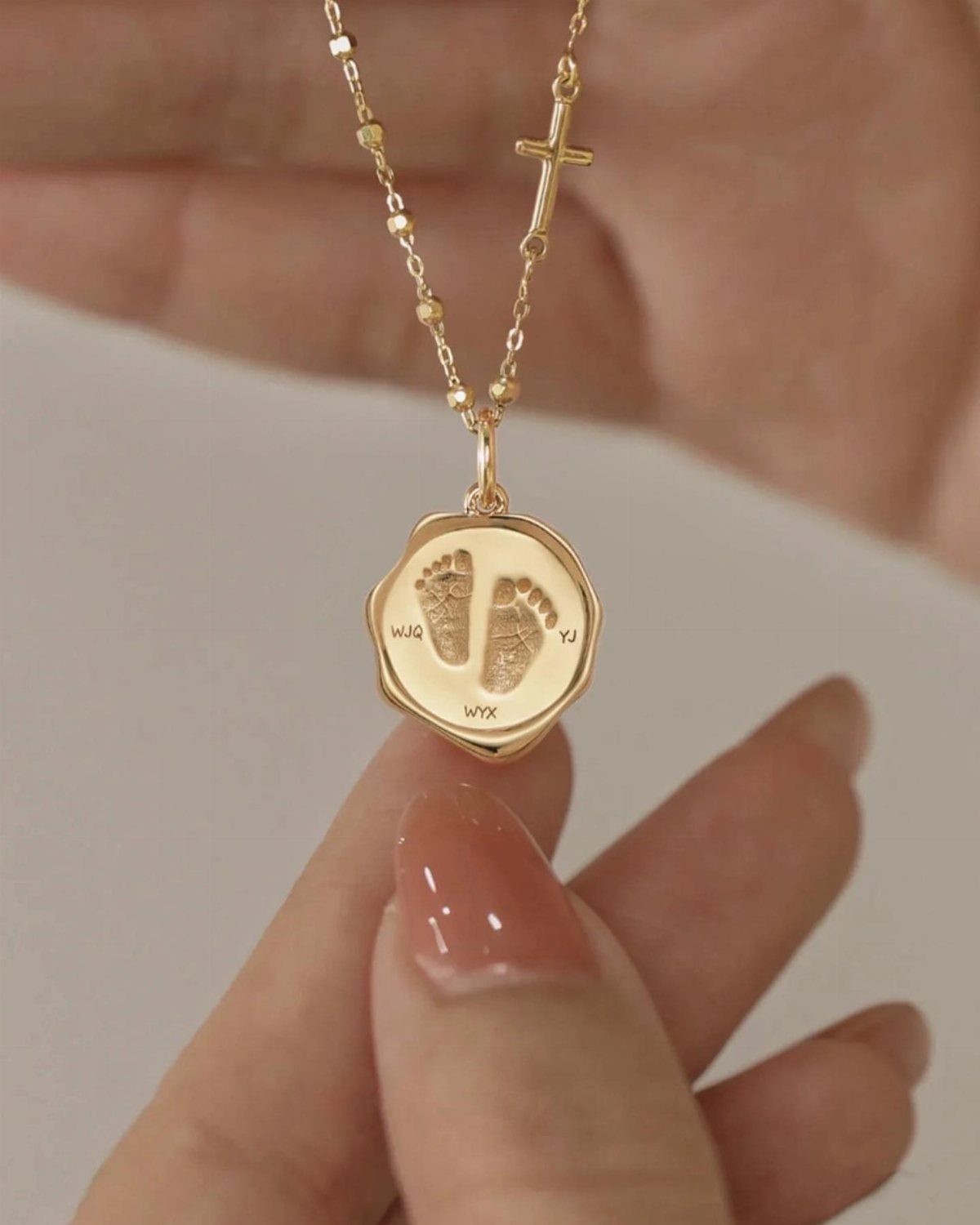 Gold necklace with a cross and a pendant engraved with baby footprints.