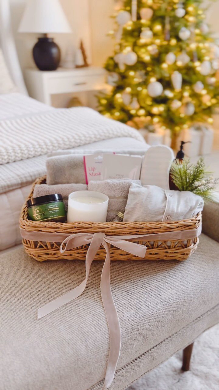 Wicker spa gift basket with candle, towels, and slippers near a Christmas tree