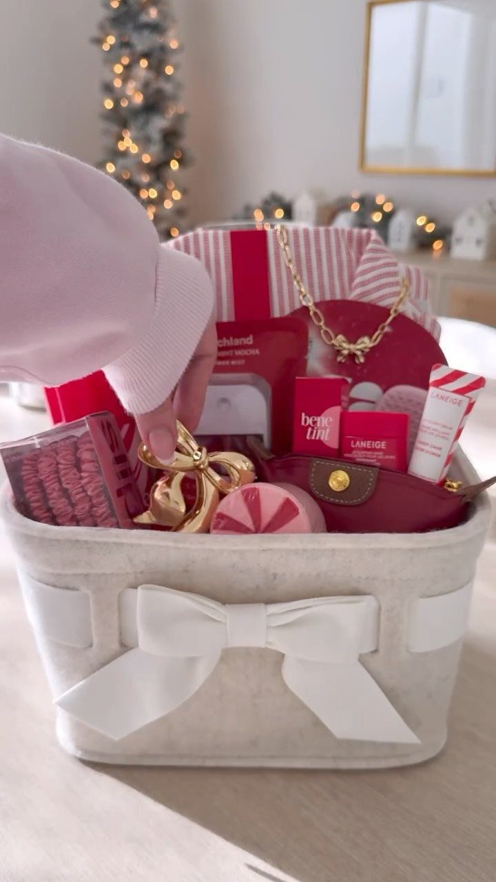 White gift basket filled with red beauty products and jewelry near a Christmas tree