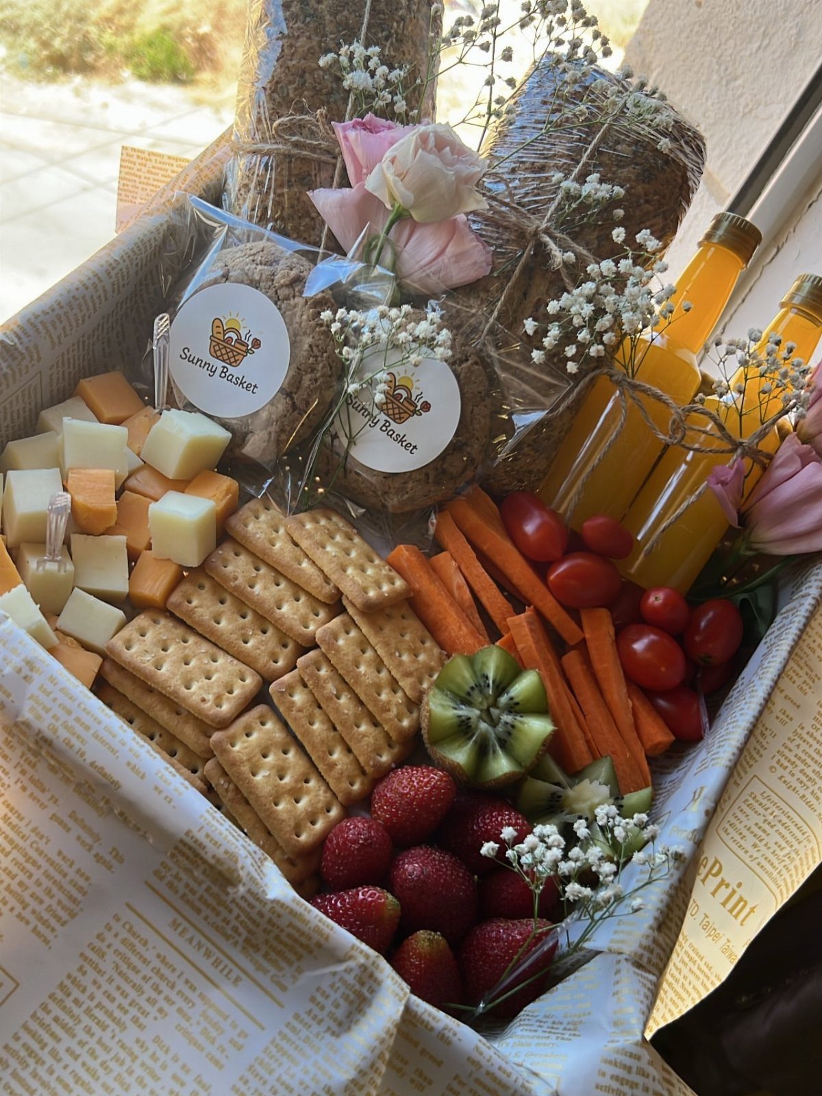 Gourmet gift basket with cheese, crackers, fresh fruit, vegetables, and orange juice bottles.
