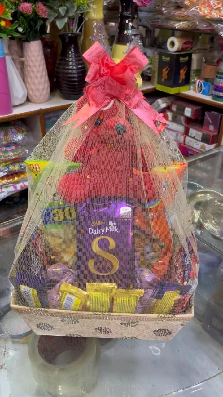 Gift basket with red teddy bear and assorted chocolates wrapped in gold tulle.