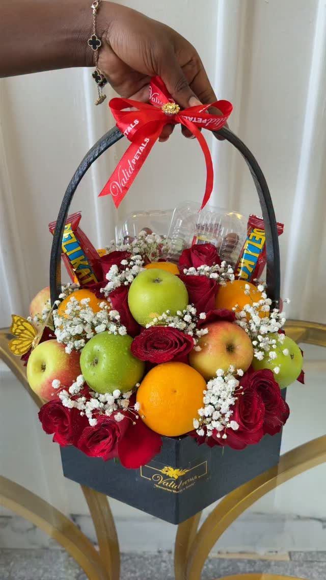 Fruit gift basket with apples, oranges, red roses, and white baby's breath flowers.