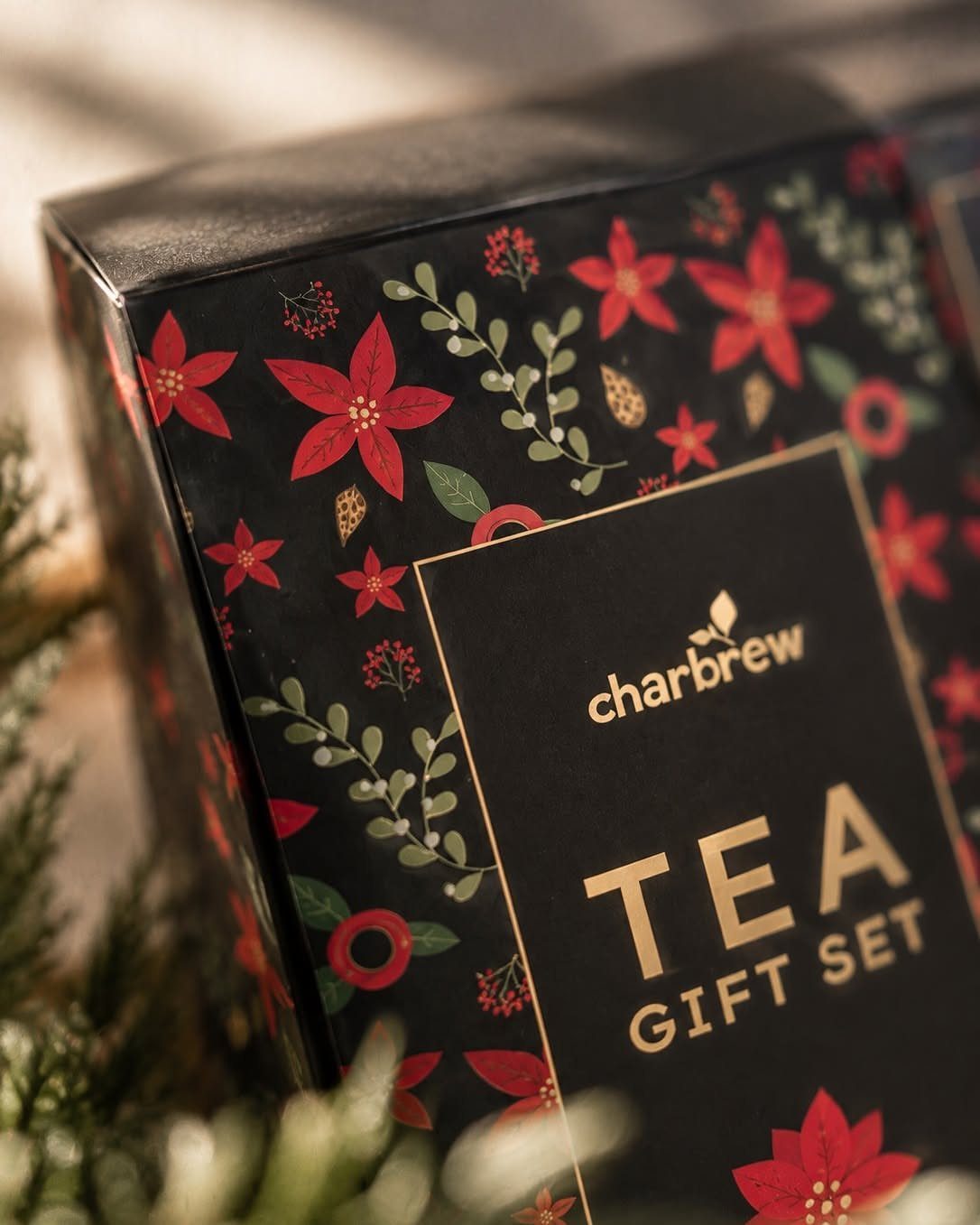 Black tea gift set box with red poinsettia patterns and gold lettering.