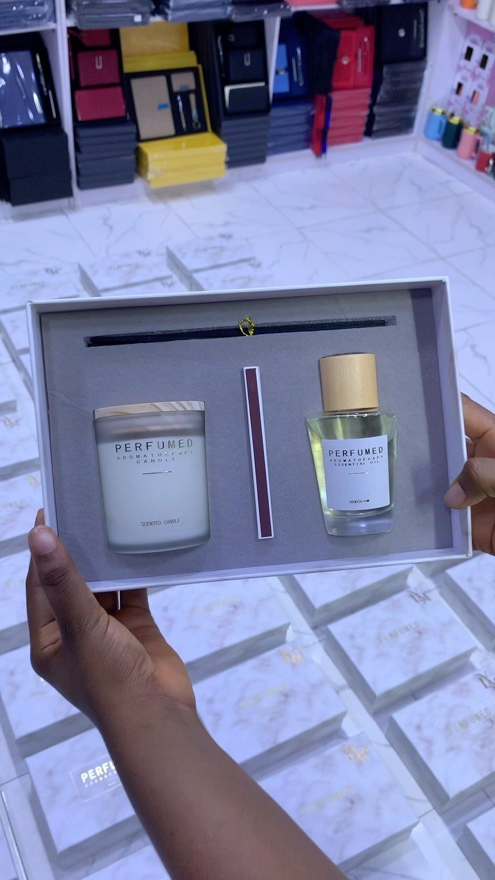 Gift box containing a scented candle and perfume held by two hands.