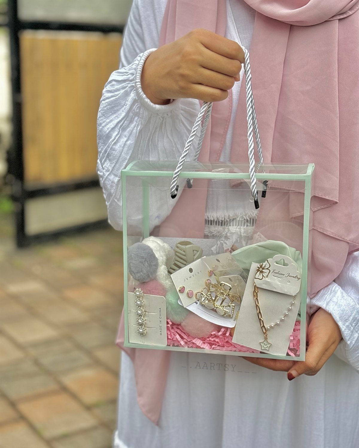 Person holding a clear acrylic gift box filled with jewelry and pink filler.