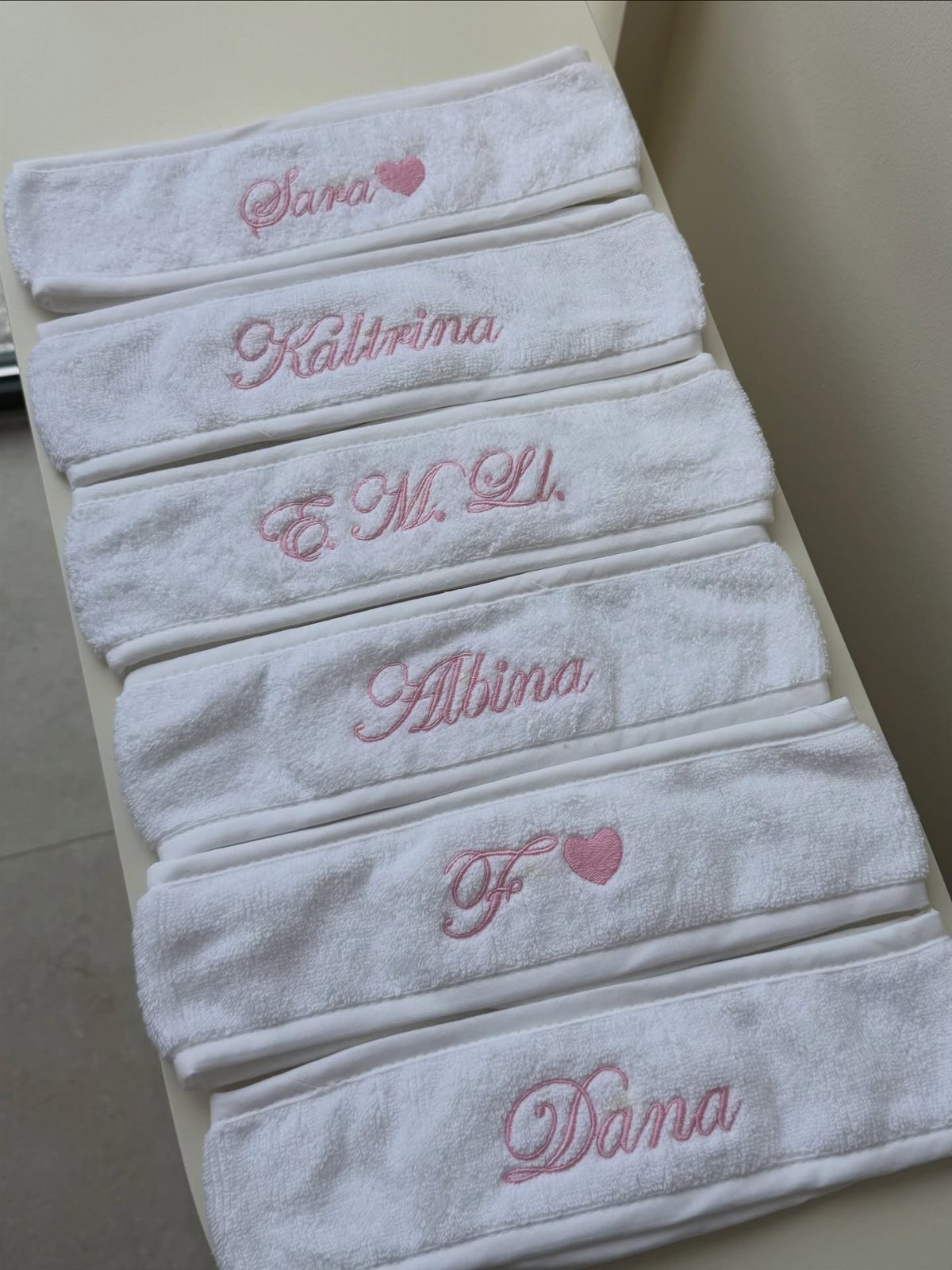 White folded towels with pink embroidered names and hearts stacked on a surface.