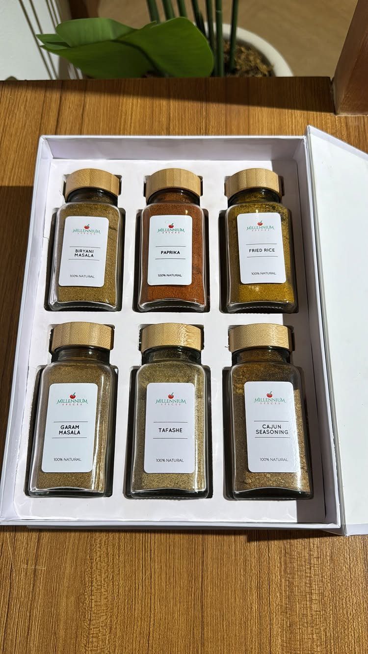 Six glass spice jars with wooden lids arranged in a white gift box.