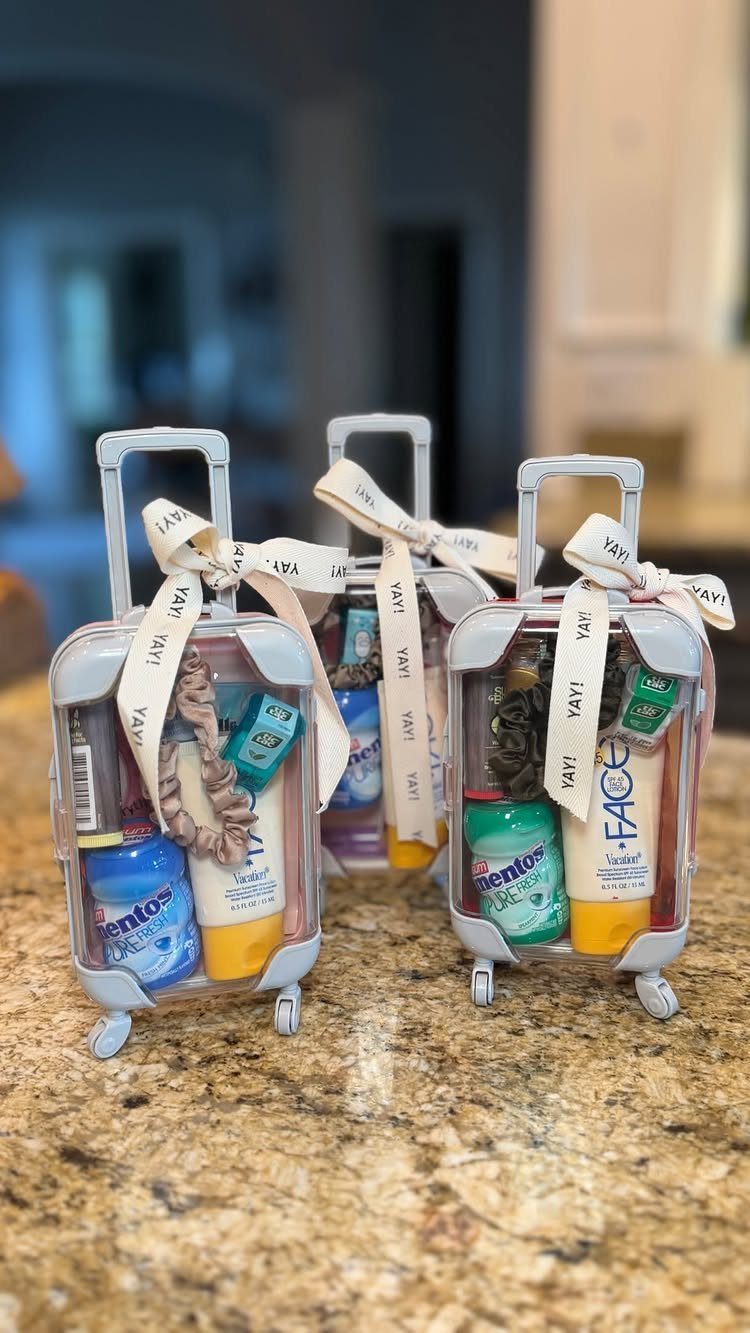 Three miniature clear suitcase gift boxes filled with toiletries on a granite surface.