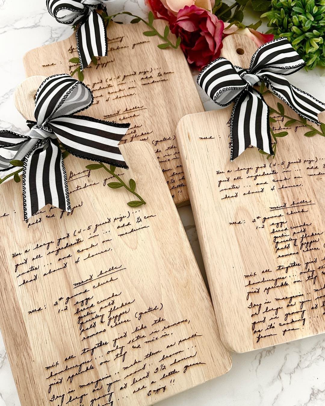 Wooden cutting boards with engraved recipes tied with black and white striped ribbons.