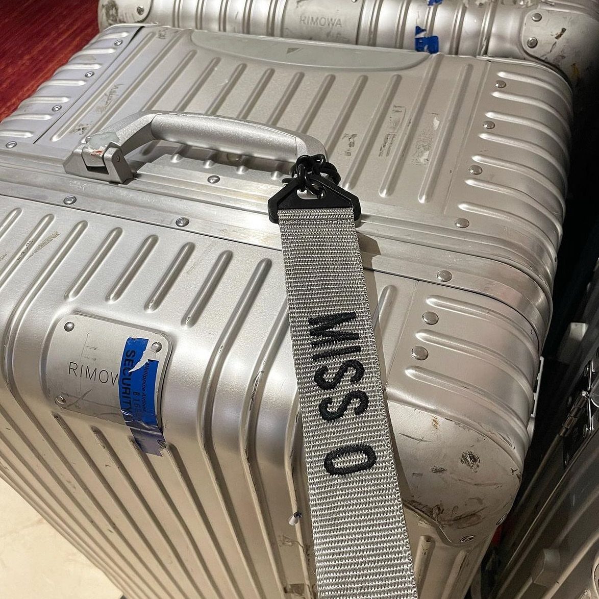 Silver aluminum suitcase with a grey personalized strap reading MISS O on the handle.