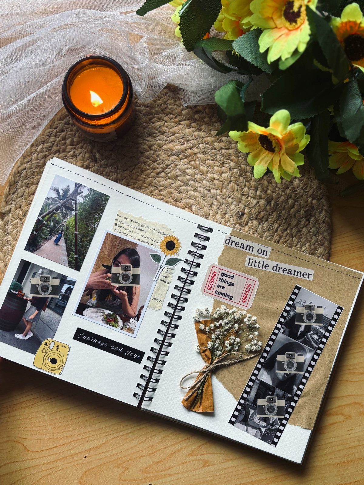 Open travel journal with photos and dried flowers next to a lit candle.