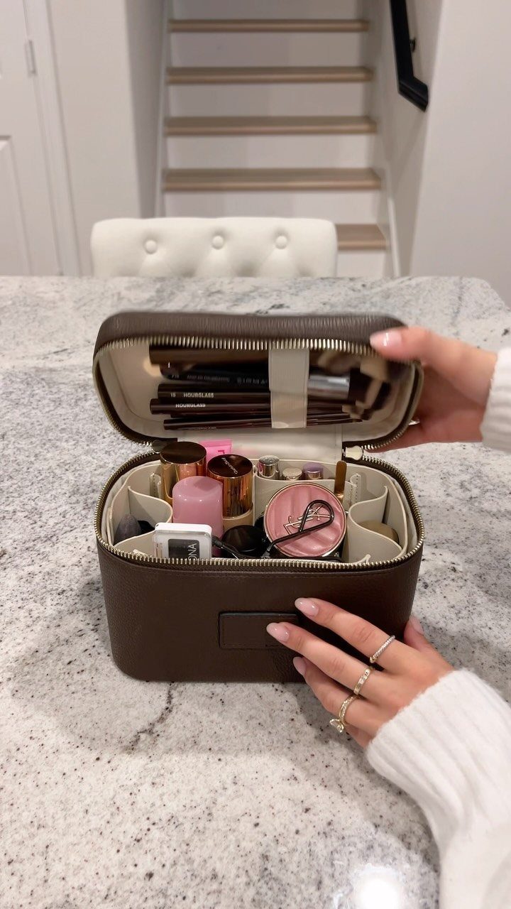 Brown travel makeup bag open and filled with cosmetics on a white counter