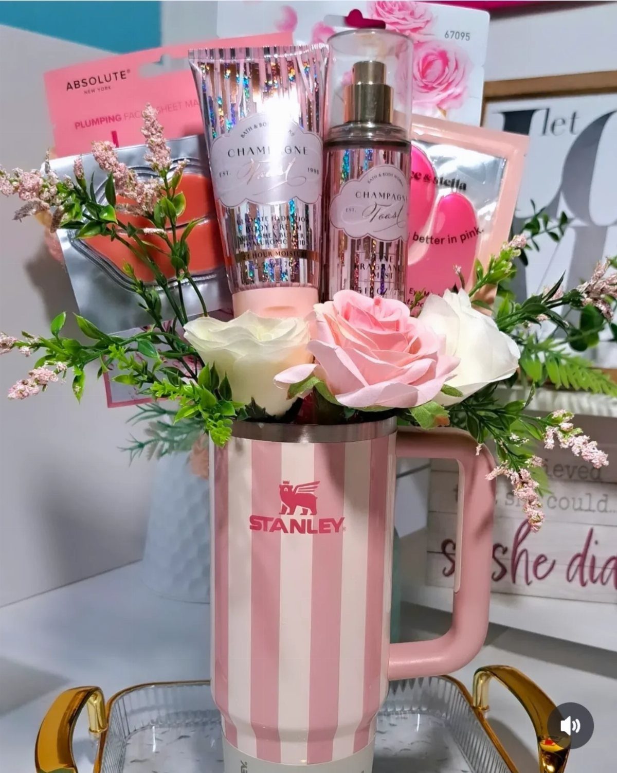Pink striped Stanley tumbler filled with roses and various beauty gift products.