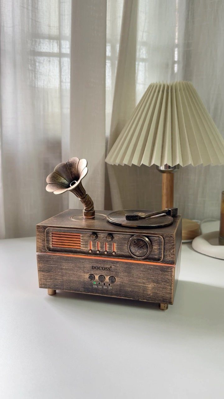 Vintage wooden record player with horn speaker next to a pleated cream lamp.