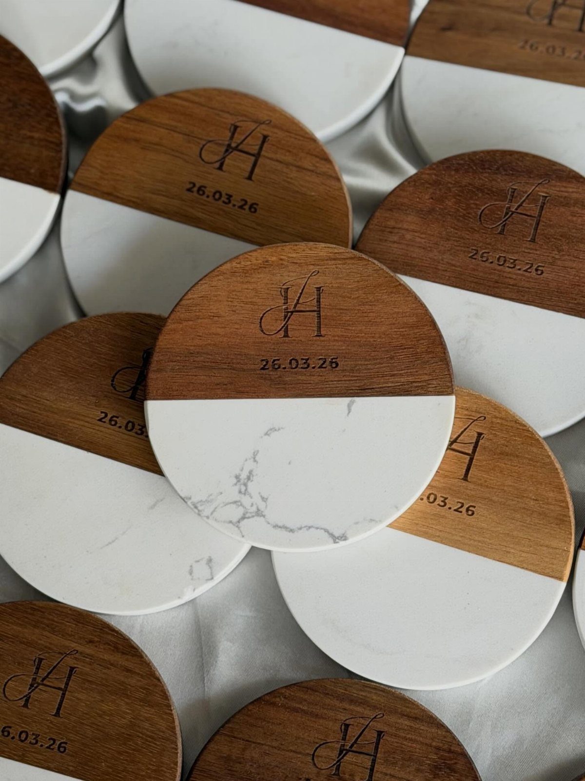 Circular monogrammed coasters made of wood and white marble with engraved initials and date.