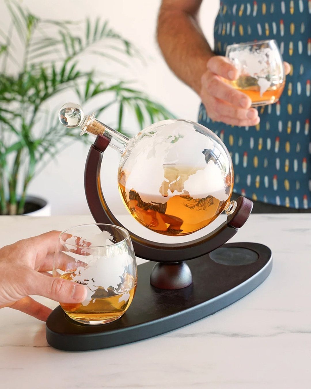 Whiskey decanter globe set with matching glasses on a white marble tabletop.