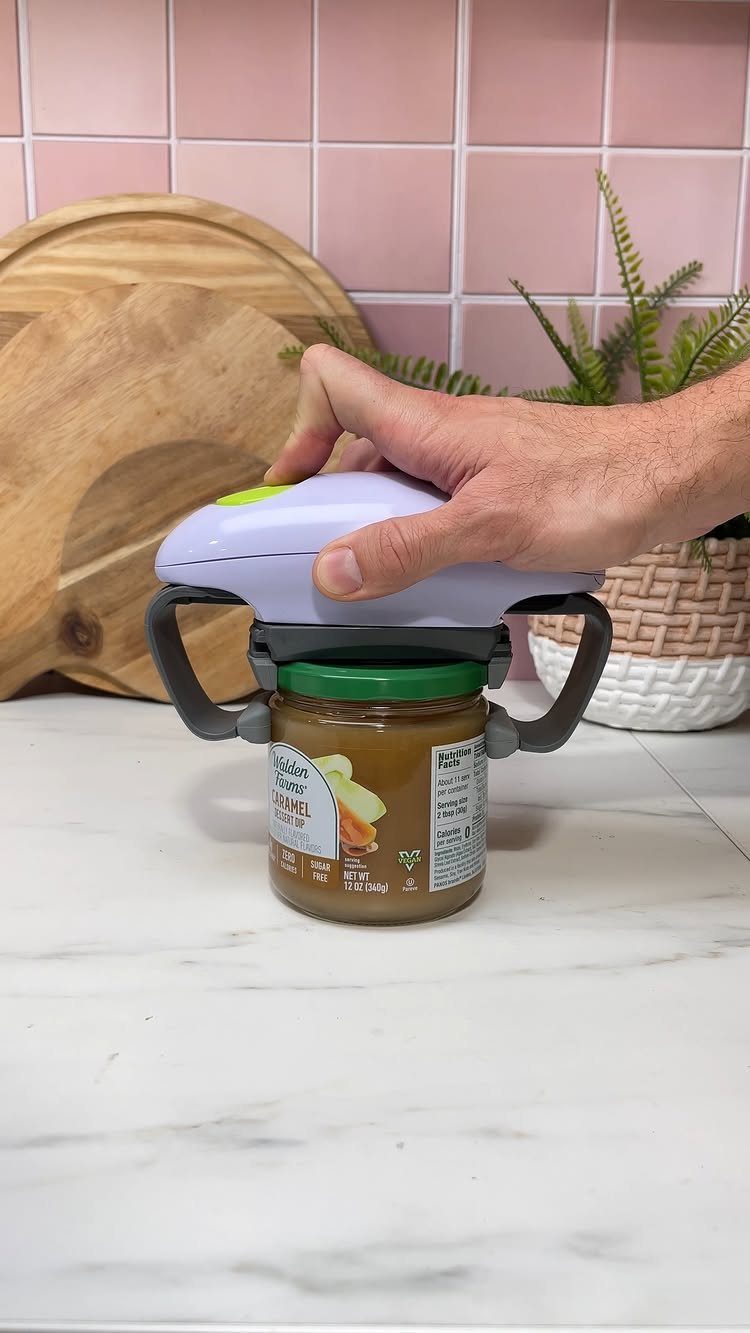 Electric jar opener removing a green lid from a glass jar on marble.