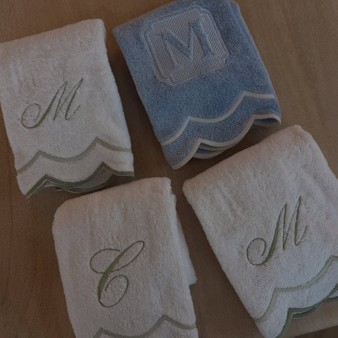 Four folded personalized dish towels with embroidered initials on a wooden table.
