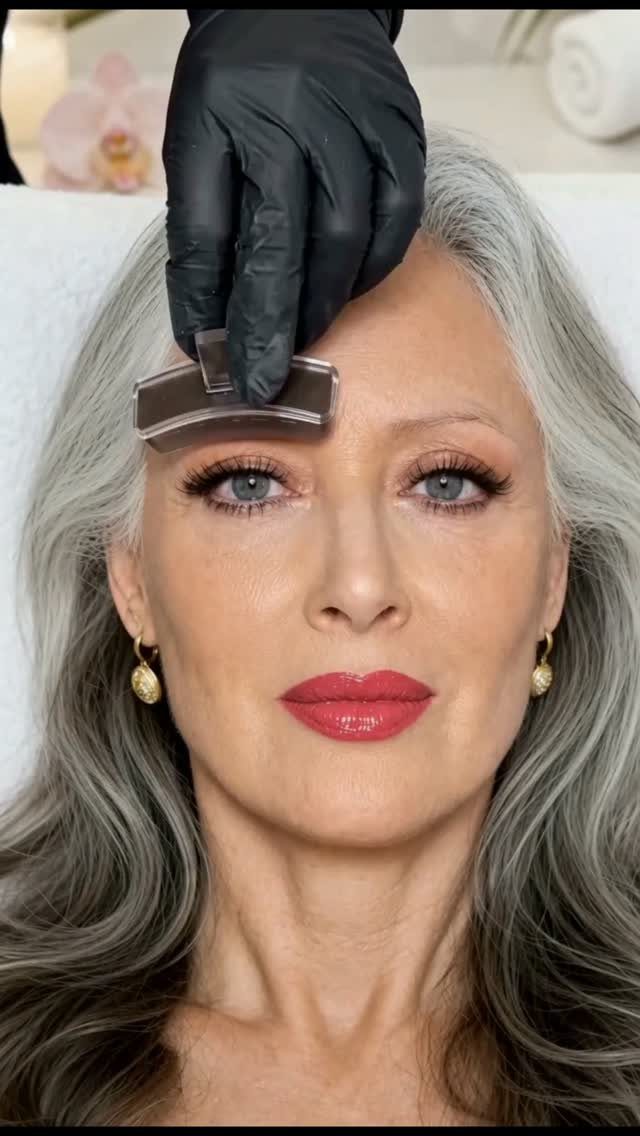 Woman with grey hair receiving a facial treatment with a metal tool.