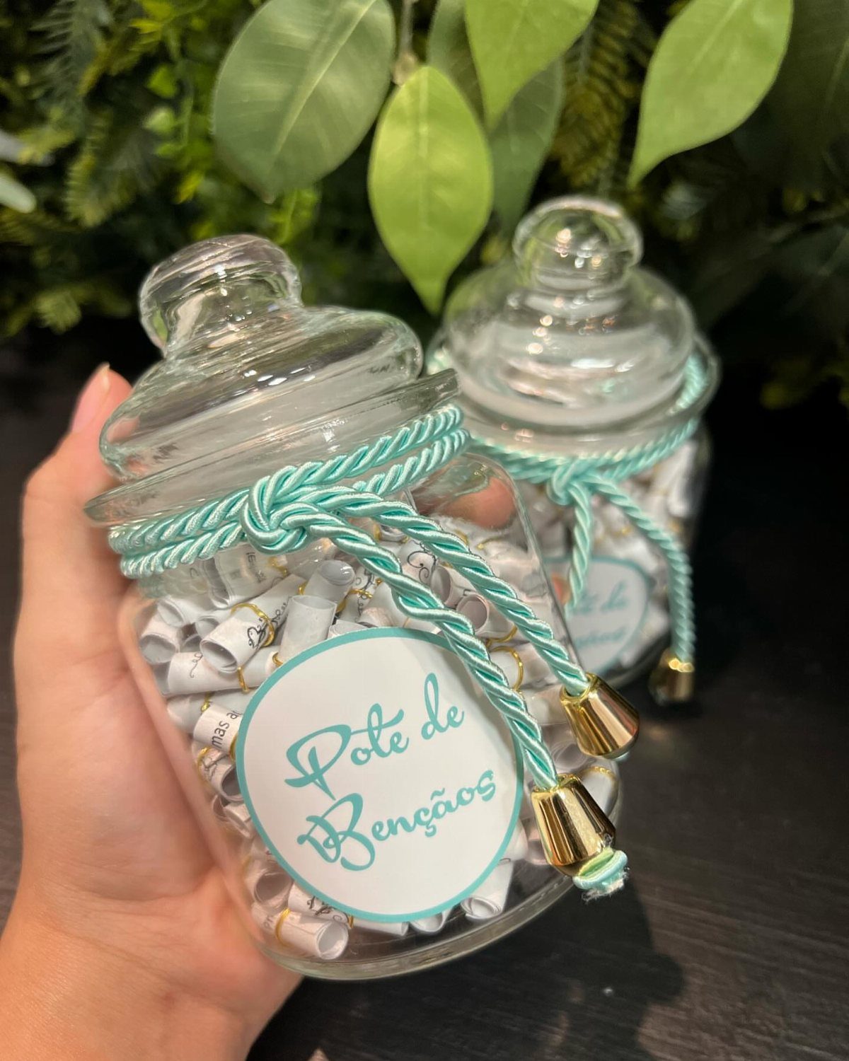 Glass jar filled with rolled white notes, decorated with turquoise cord and gold bells.