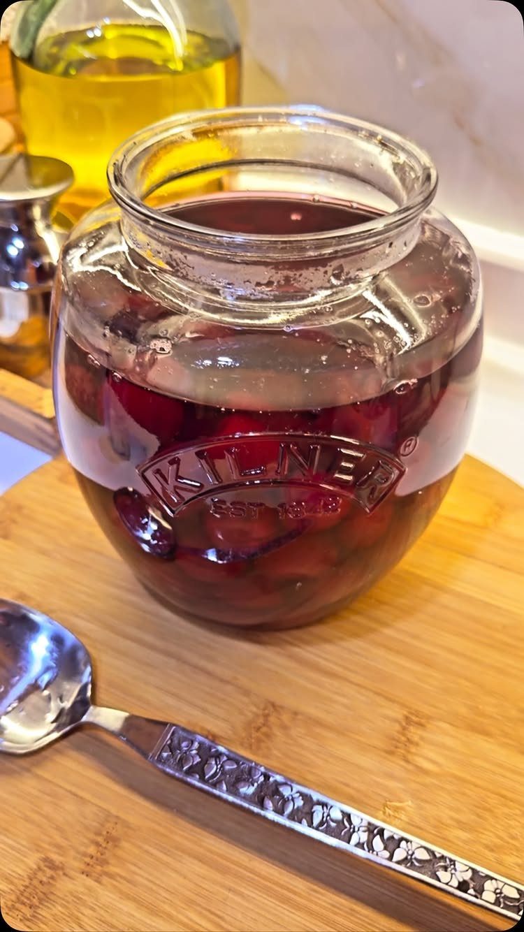 Dark red cherries in a glass Kilner jar on a wooden cutting board.