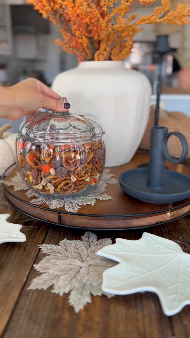 Glass jar filled with autumn snack mix on a wooden tray with leaves.