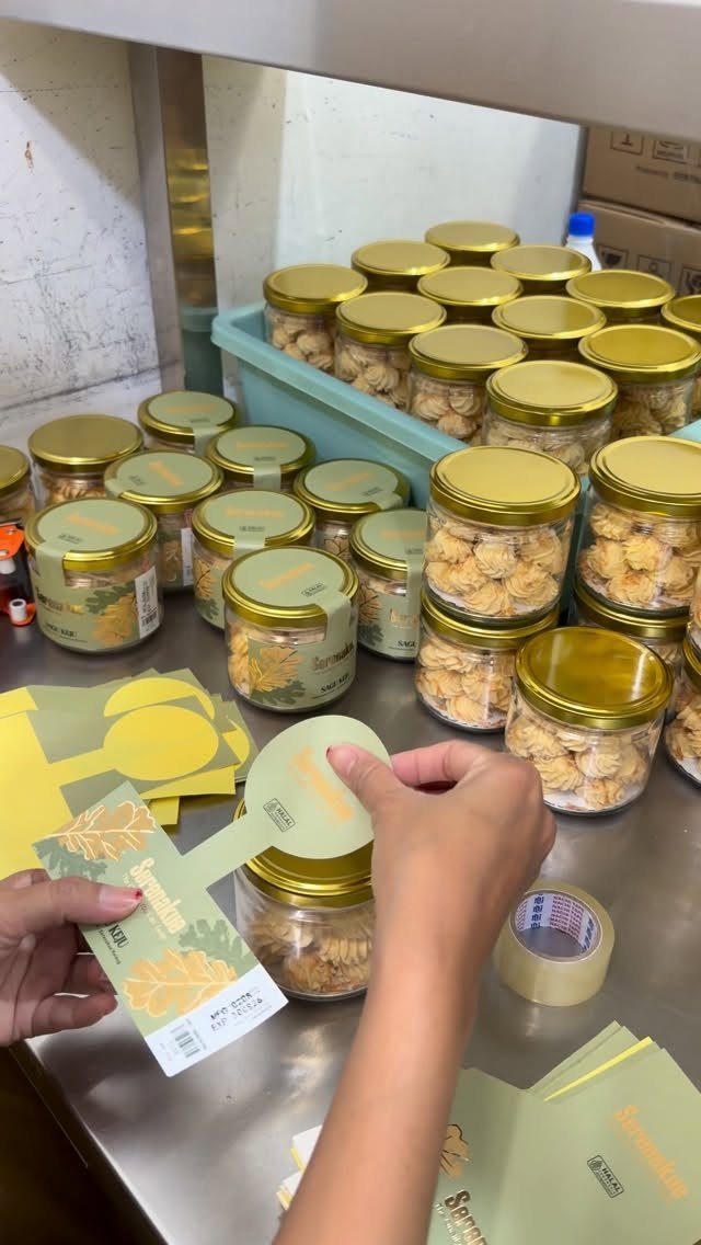 Glass jars filled with golden-brown cookies being labeled by hand on a table.