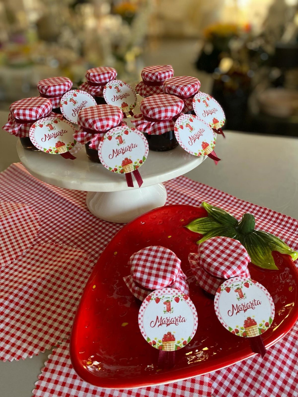Small jam jars with checkered fabric lids and tags on a white stand.