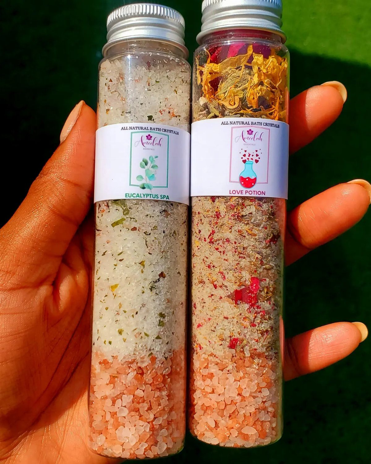 Two glass jars filled with layered bath salts and botanicals held in a hand.