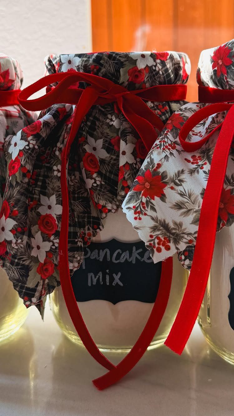 Mason jars filled with pancake mix, topped with floral fabric and red ribbons.