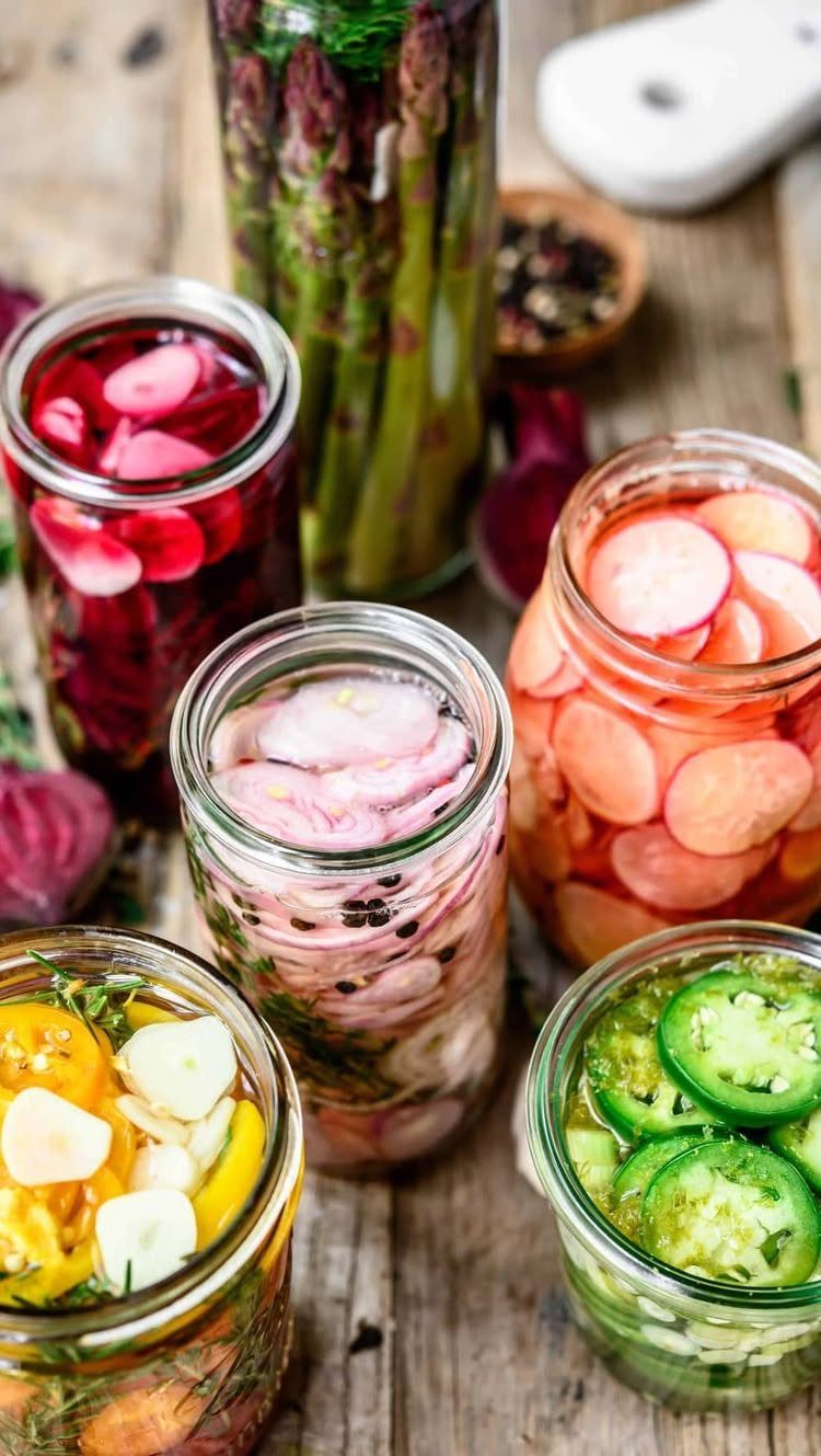 Pickled vegetables in glass mason jars on a rustic wooden table.