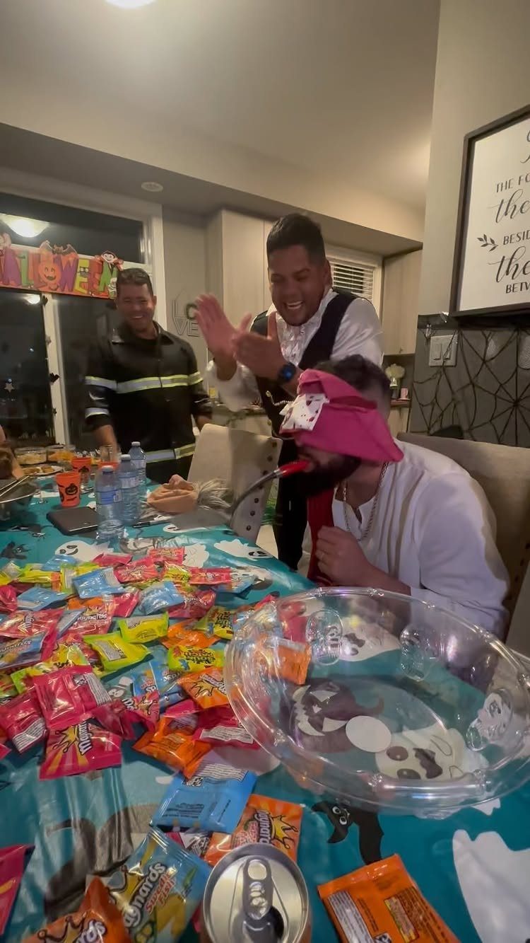 Blindfolded man sitting at a table covered in colorful Halloween candies and treats.